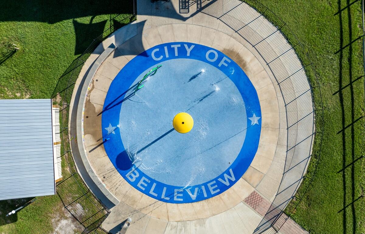 Aerial photo of the City of Belleview splash pad with blue circular design, yellow water feature, and surrounding pavement and grass.