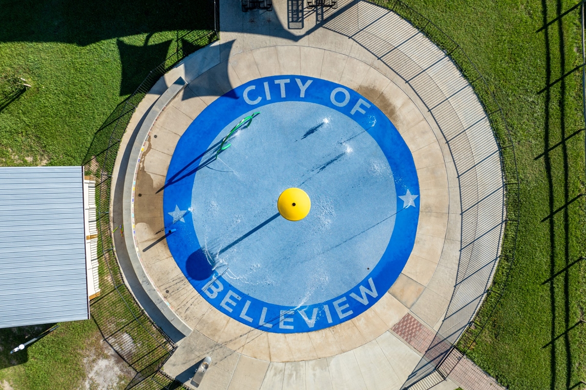 Aerial photo of the City of Belleview splash pad with blue circular design, yellow water feature, and surrounding pavement and grass.