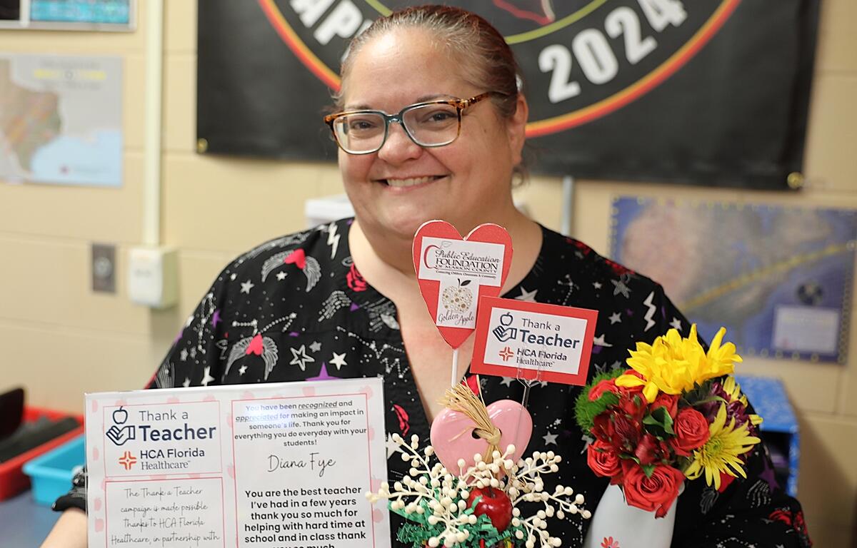 Diana Fye smiles while holding her “Thank a Teacher” award certificate and flowers, presented by HCA Florida Healthcare and the Public Education Foundation.