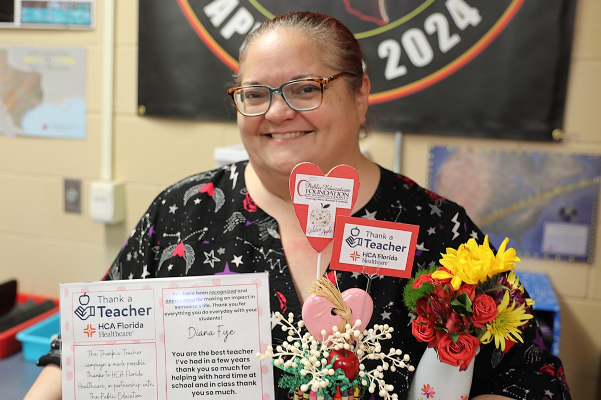 Diana Fye smiles while holding her “Thank a Teacher” award certificate and flowers, presented by HCA Florida Healthcare and the Public Education Foundation.
