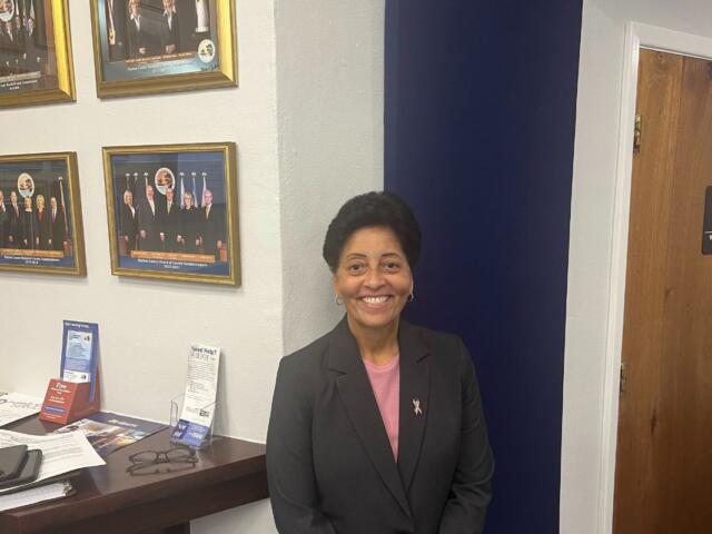 A professionally dressed woman with short hair standing in front of a wall and door.