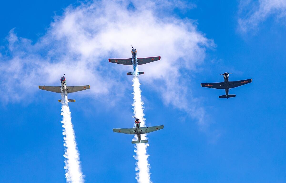 Four military aircraft fly in formation against a blue sky with white smoke trails during a Memorial Day flyover.