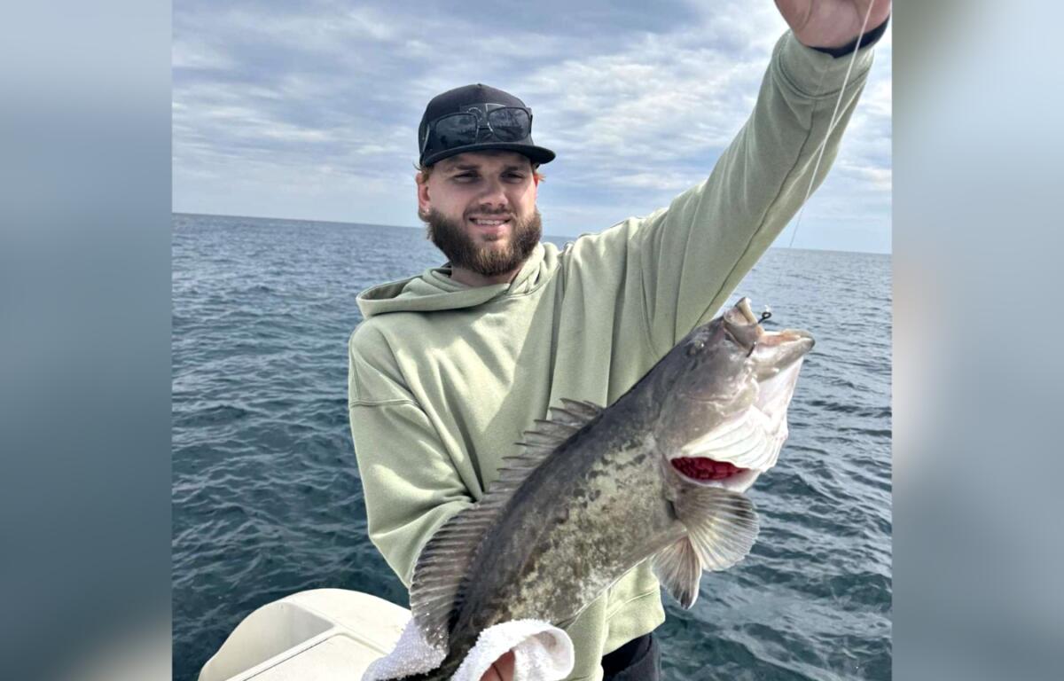 Man holding a large fish on a boat in the ocean under a cloudy sky