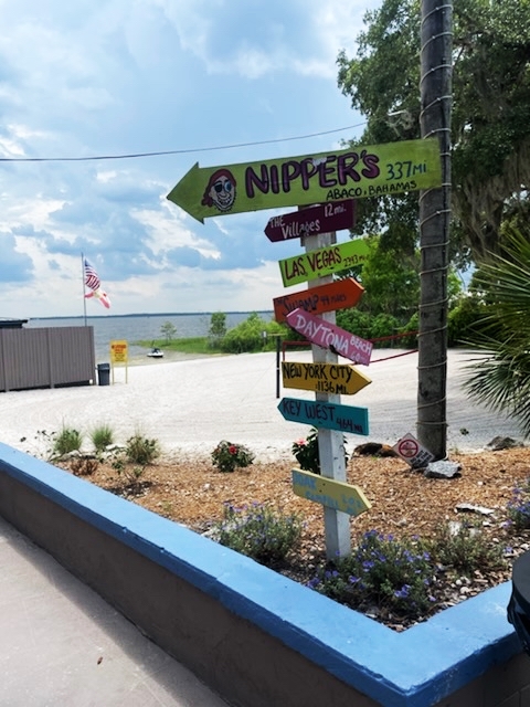 Directional signpost at Gator Joe’s with arrows pointing to various destinations like The Villages, Las Vegas, Daytona Beach, and Key West, with Lake Weir visible in the background