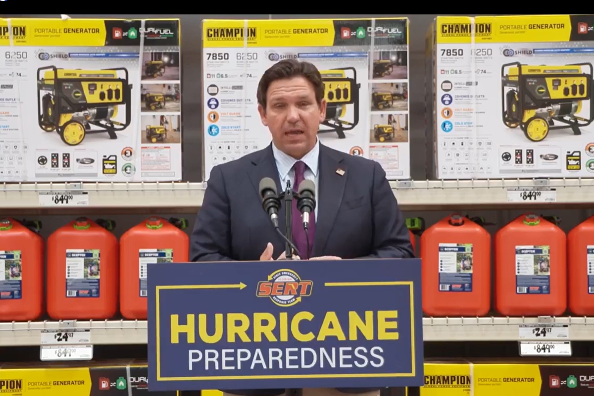Florida Gov. Ron DeSantis stands at a podium labeled “Hurricane Preparedness” inside a Home Depot, with gas cans and portable generators on display behind him.