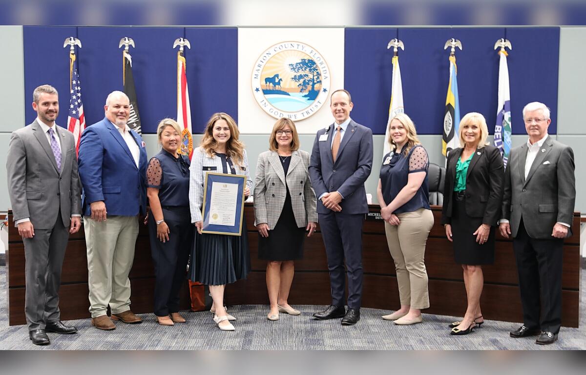 Group photo of Marion County commissioners and hospital representatives standing in front of the county seal and flags, with one woman holding a framed proclamation recognizing National Nurses Week and National Hospital Week.