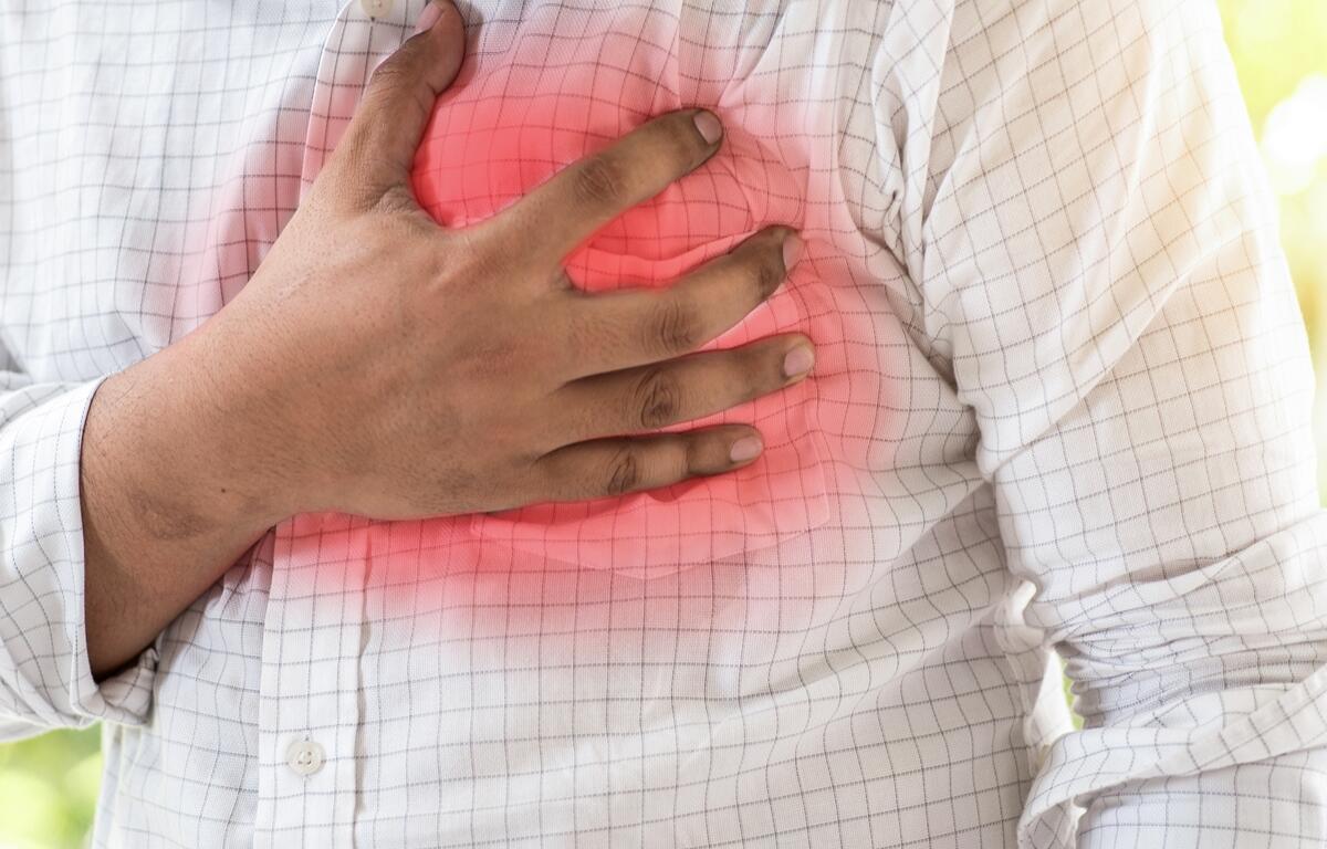 A person wearing a checkered shirt clutches their chest in pain, highlighting symptoms of sudden cardiac arrest.