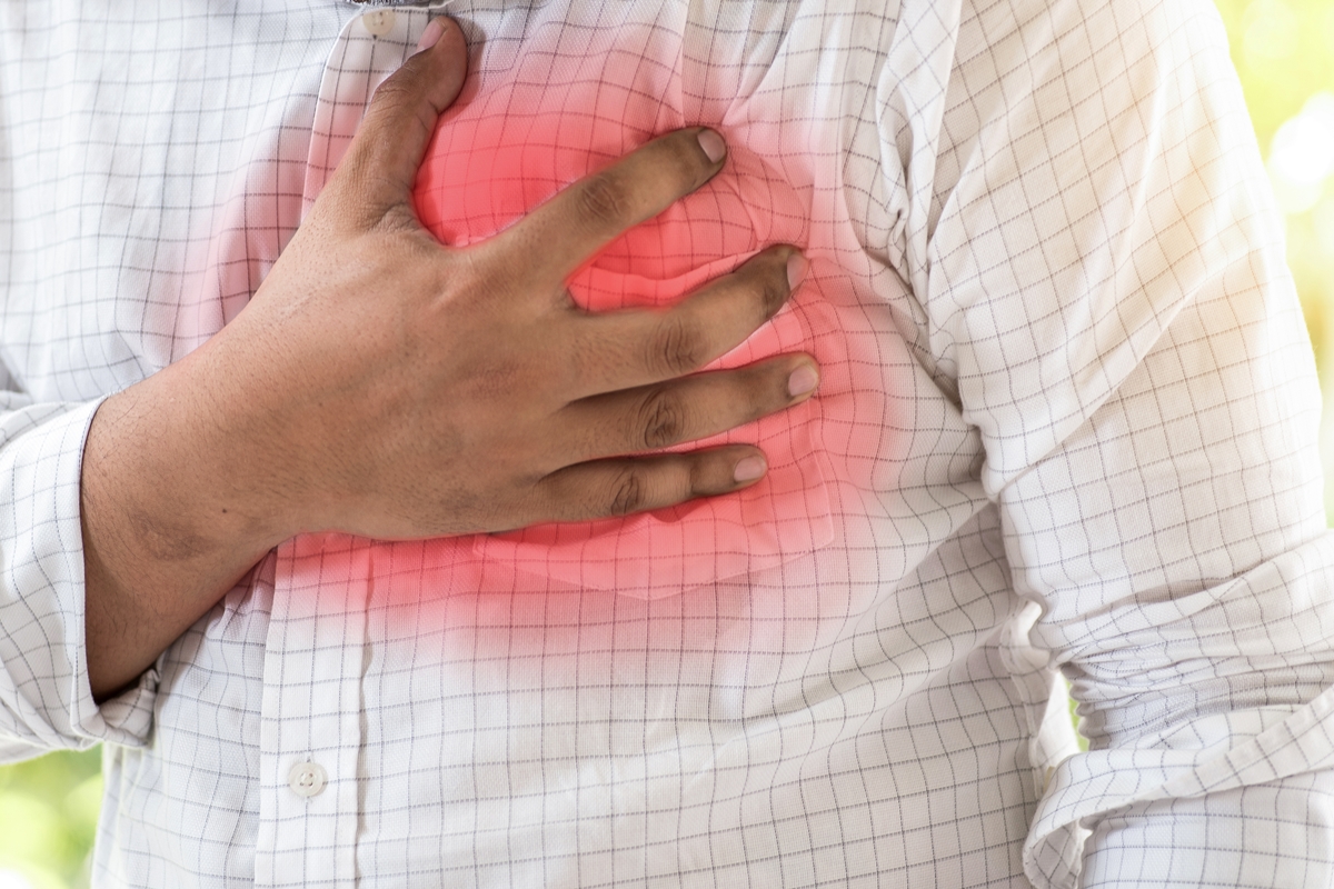 A person wearing a checkered shirt clutches their chest in pain, highlighting symptoms of sudden cardiac arrest.