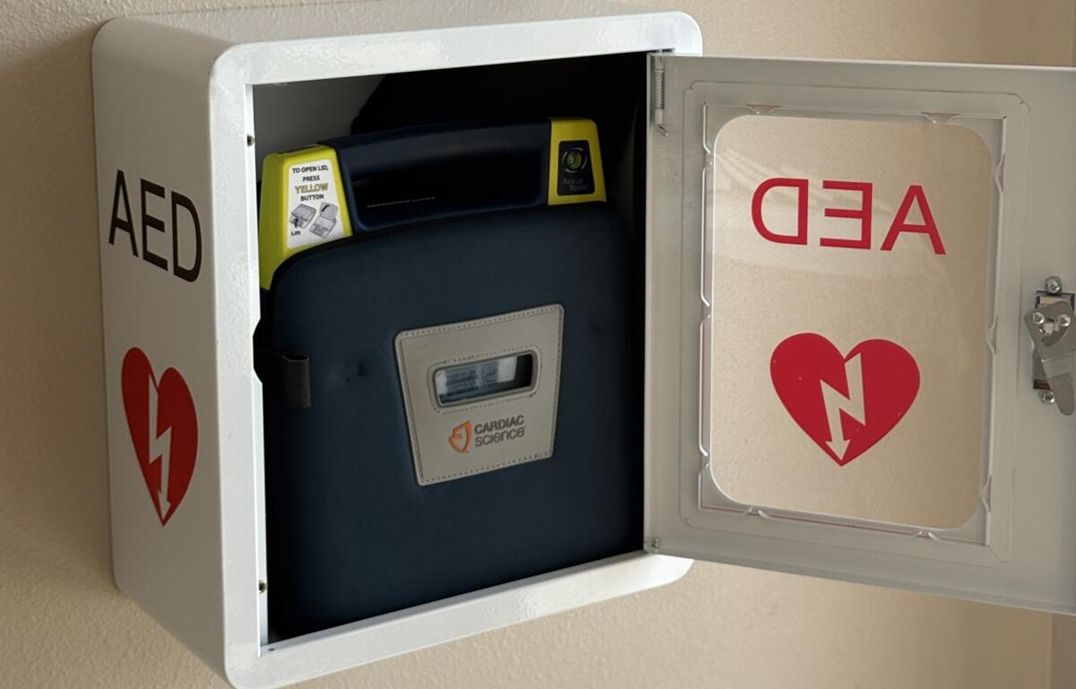 An automated external defibrillator (AED) in a white wall-mounted cabinet with the door open, located at the Belleview Community Center.