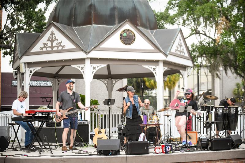 Heather Lynne performs with her full band on the gazebo stage in downtown Ocala, surrounded by instruments and equipment during an outdoor concert.