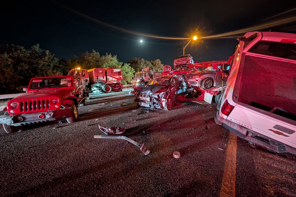 Damaged car hauler with crushed cab and dislodged vehicles leans against a guardrail after a crash on I-75 in Ocala at night.