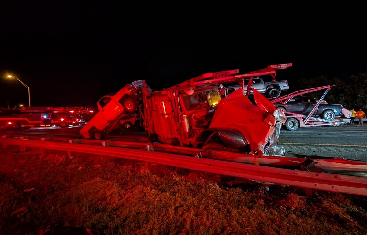 Damaged car hauler with crushed cab and dislodged vehicles leans against a guardrail after a crash on I-75 in Ocala at night.