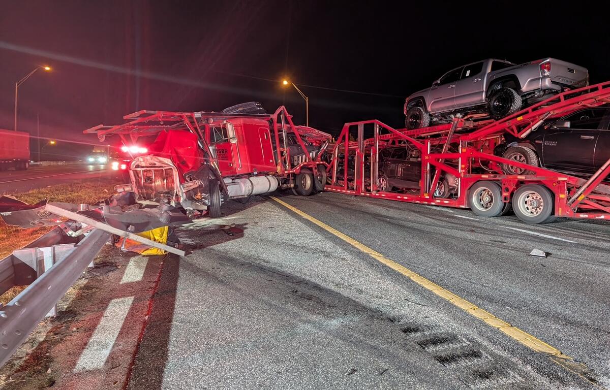 Red car hauler with visible front-end damage rests on I-75 near a damaged guardrail following a multi-vehicle crash in Ocala.