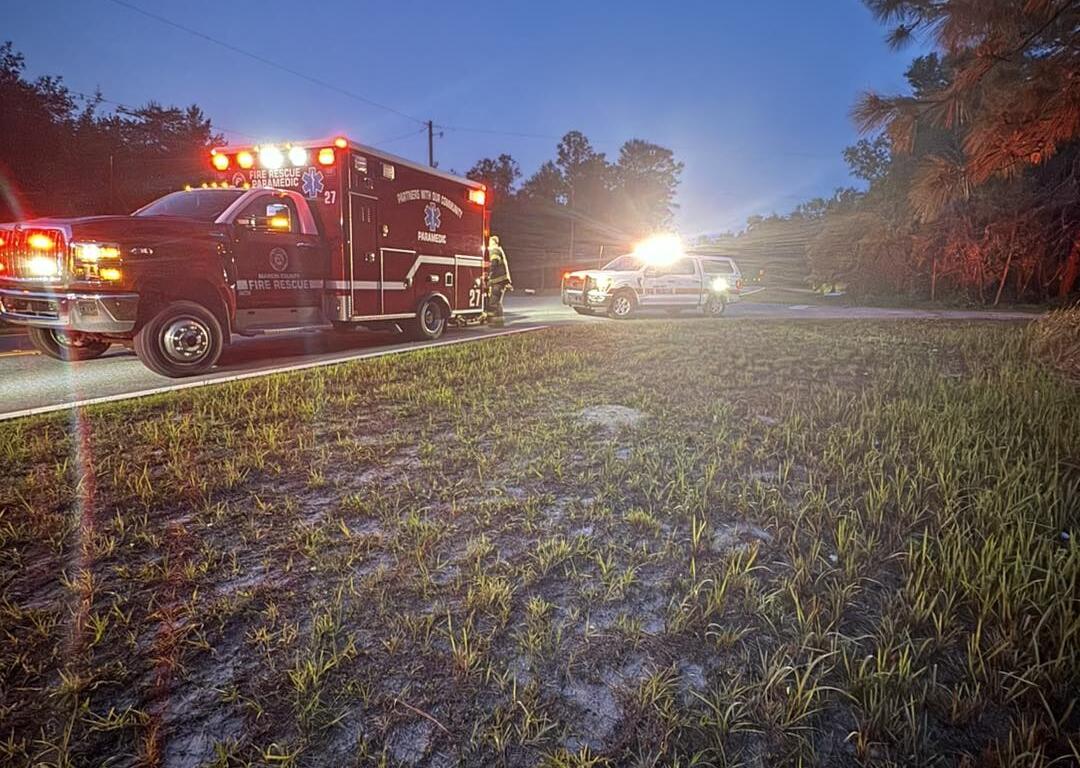 Emergency vehicles with flashing lights parked on a rural road at dawn, including an MCFR ambulance and command SUV, with moon visible in early morning sky.