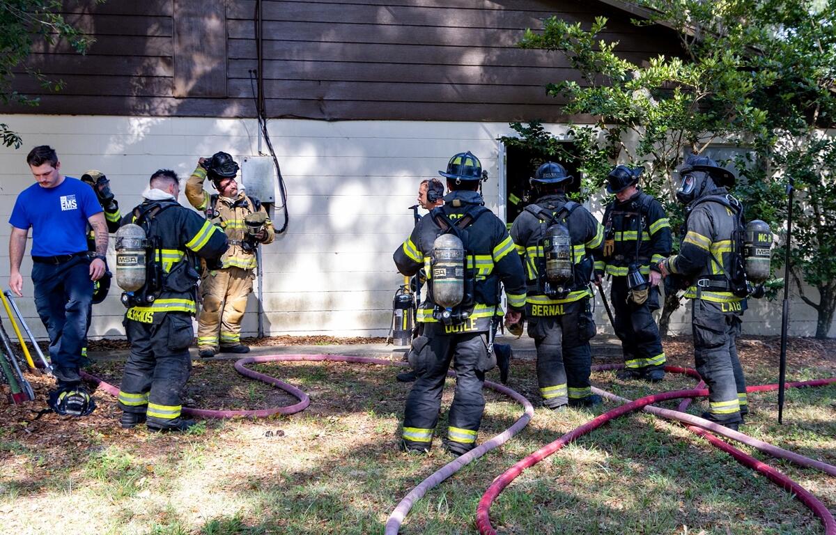 Marion County firefighters in full gear standing outside a quadraplex with hoses on the ground after putting out a fire.