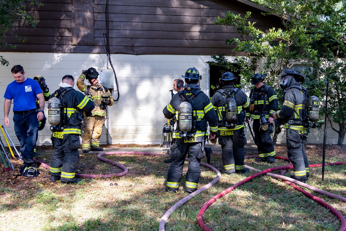 Marion County firefighters in full gear standing outside a quadraplex with hoses on the ground after putting out a fire.