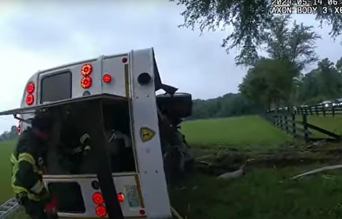 Firefighter inspects overturned bus in grassy field after fatal crash in Marion County, Florida.