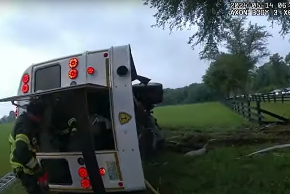 Firefighter inspects overturned bus in grassy field after fatal crash in Marion County, Florida.