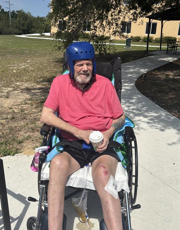 Lynn's husband, Don, sits in a wheelchair with a blue helmet on and a pink shirt.