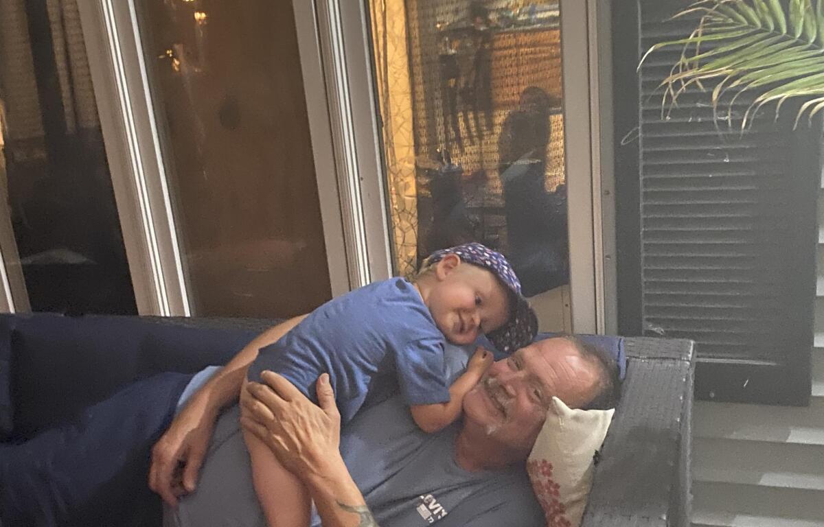 Don lounges on a couch with his grandson, Cameron, who is wearing a blue ballcap and a blue shirt
