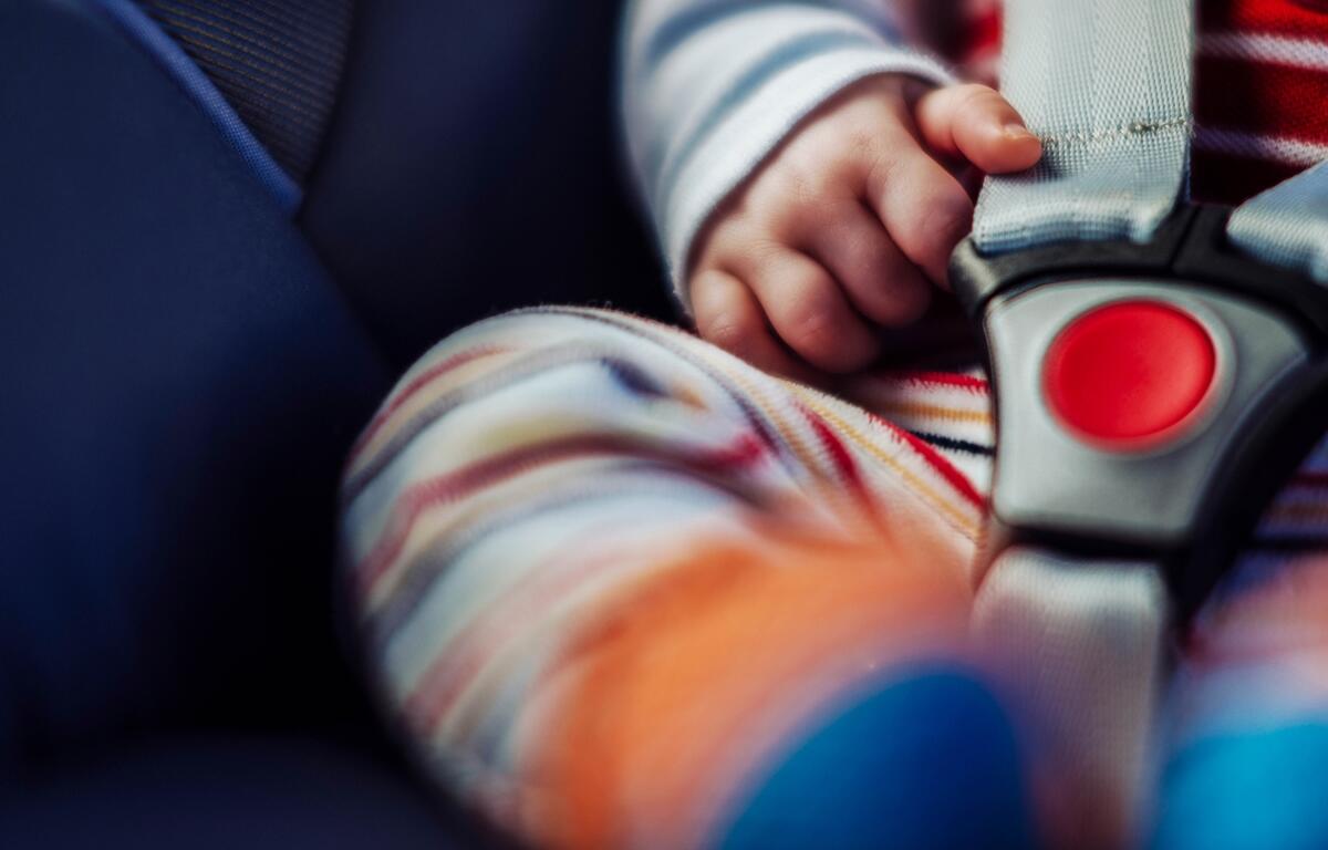 A child’s hand rests on a car seat harness, a visual reminder of the importance of checking the back seat—especially on National Heatstroke Prevention Day, May 1.
