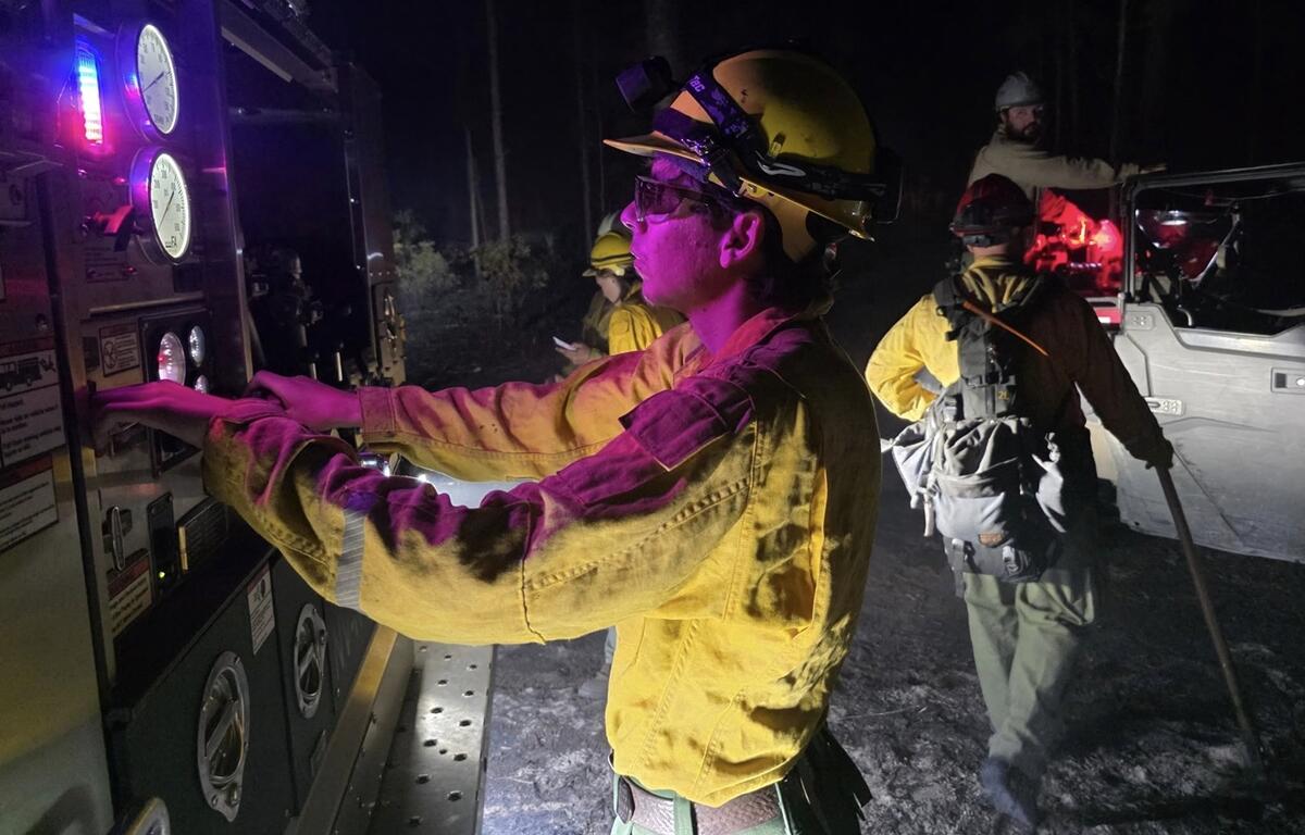 Firefighter in yellow gear adjusts engine controls at night while others work nearby during wildfire response in the Ocala National Forest.