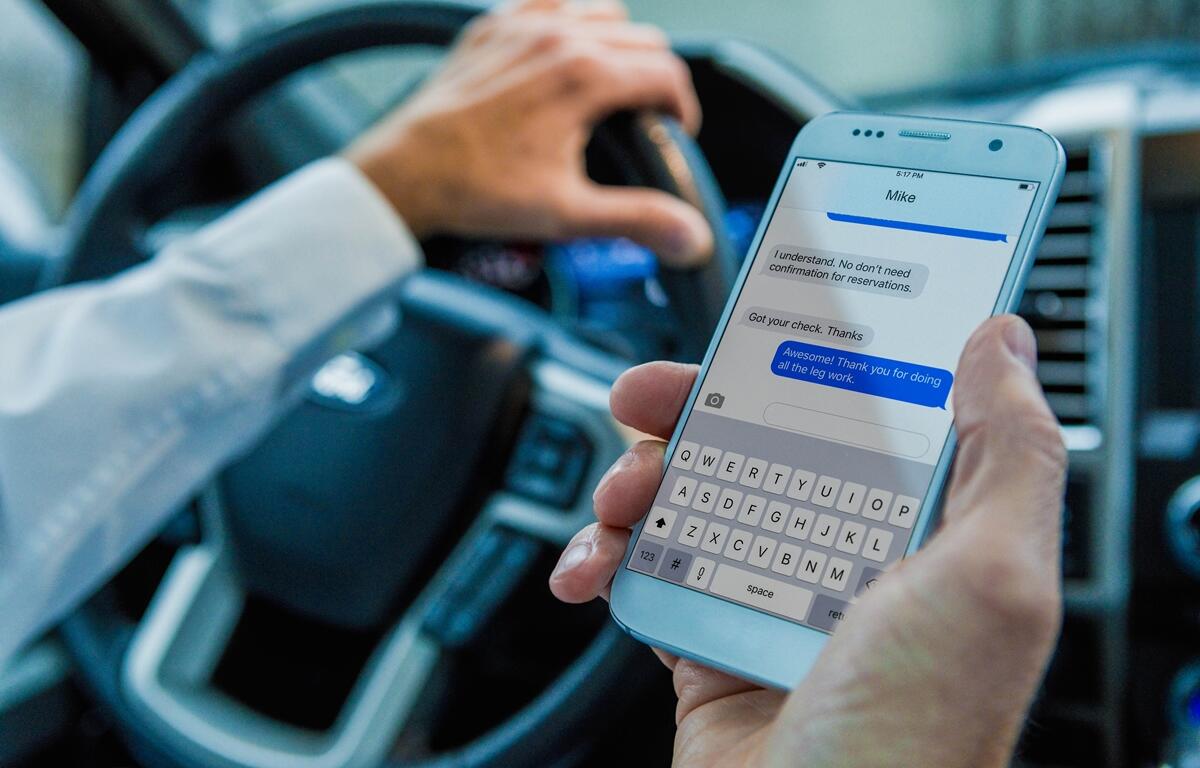 Close-up of a person texting on a smartphone while driving a vehicle.
