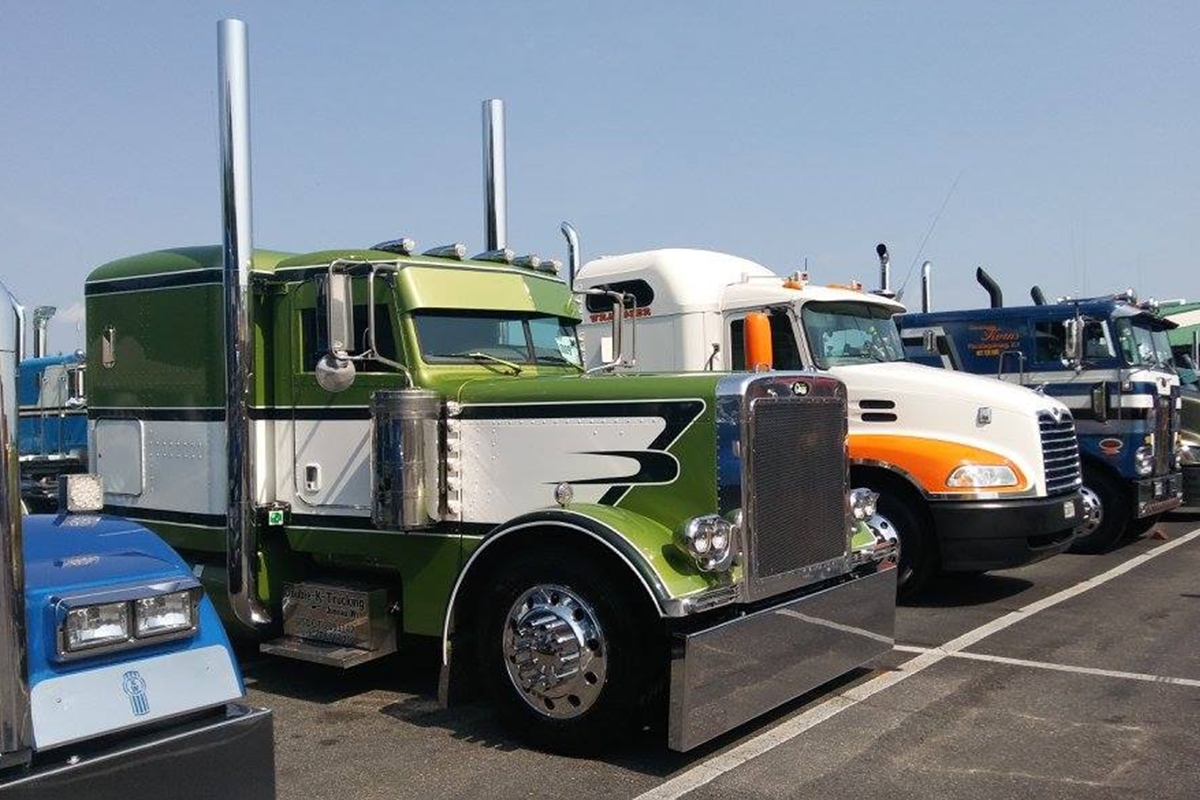 Row of colorful custom semi-trucks parked in a lot, including green, white, and blue designs, displayed for a truck show competition.