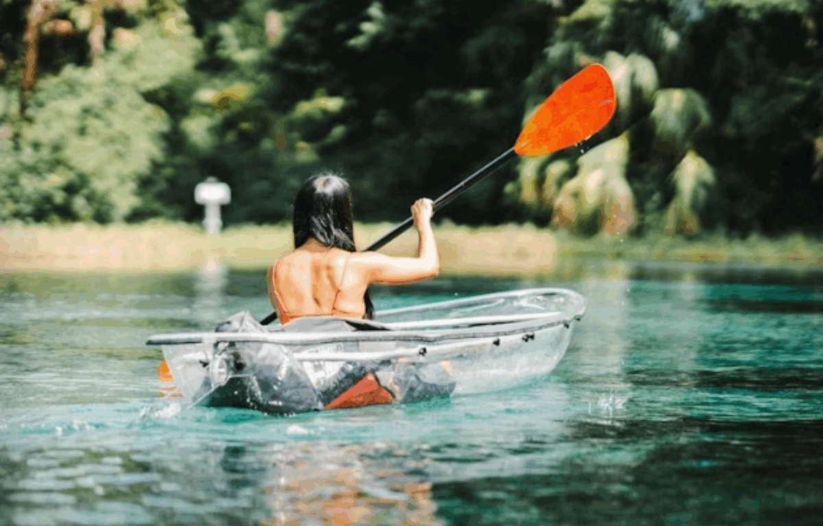 Person paddling a clear kayak on crystal-blue water surrounded by lush greenery in Marion County.