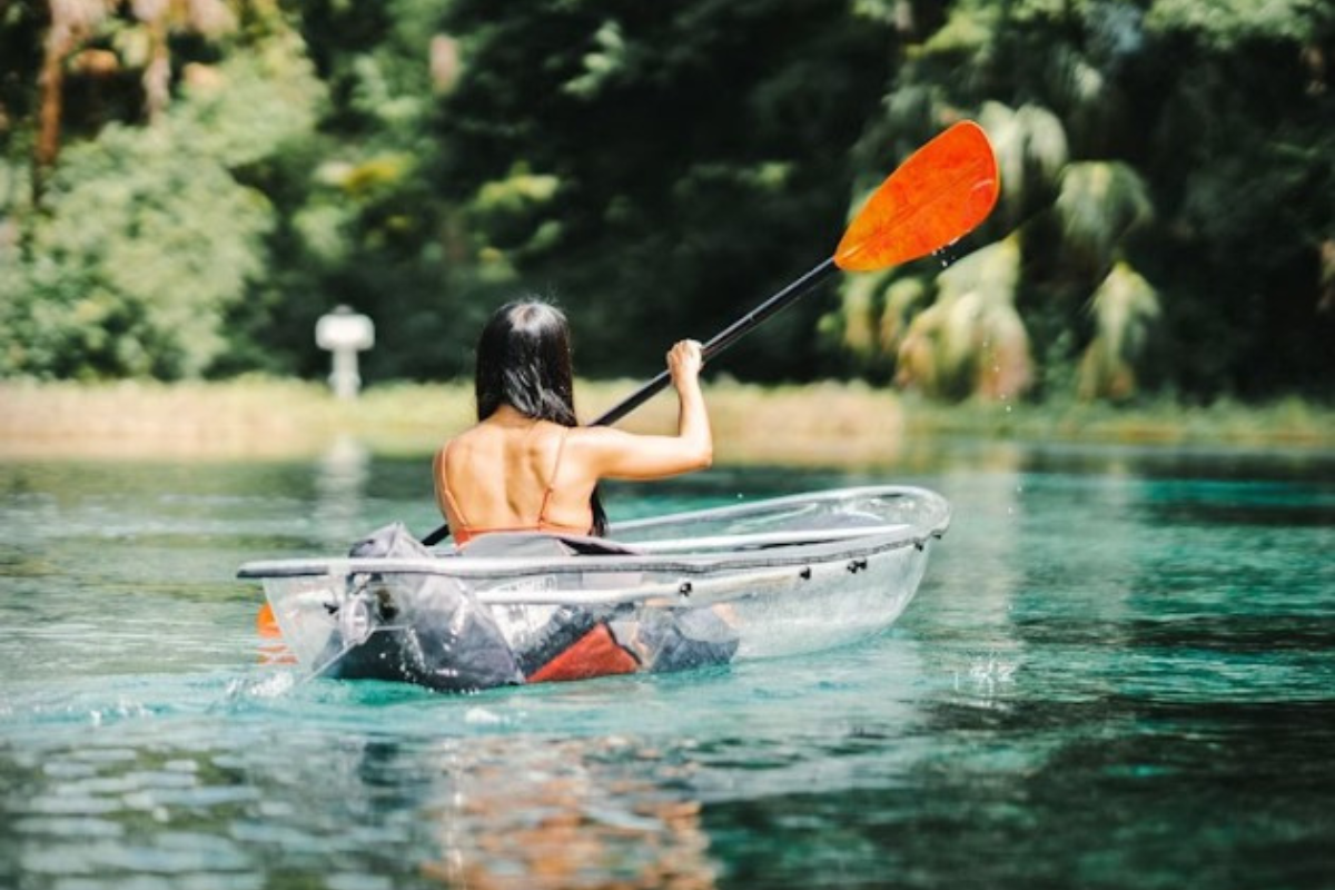 Person paddling a clear kayak on crystal-blue water surrounded by lush greenery in Marion County.
