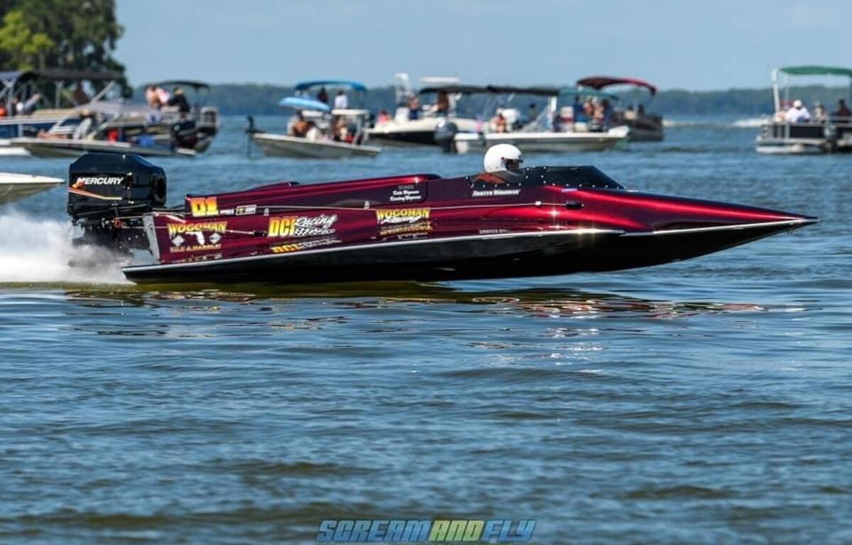 A sleek maroon drag boat speeds across Lake Eustis with other boats and spectators visible in the background.