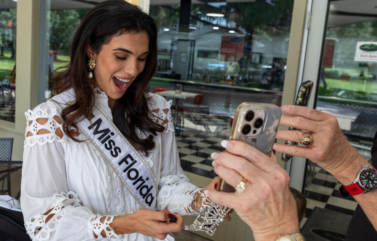 Miss Florida smiling and holding her crown while interacting with people taking photos.