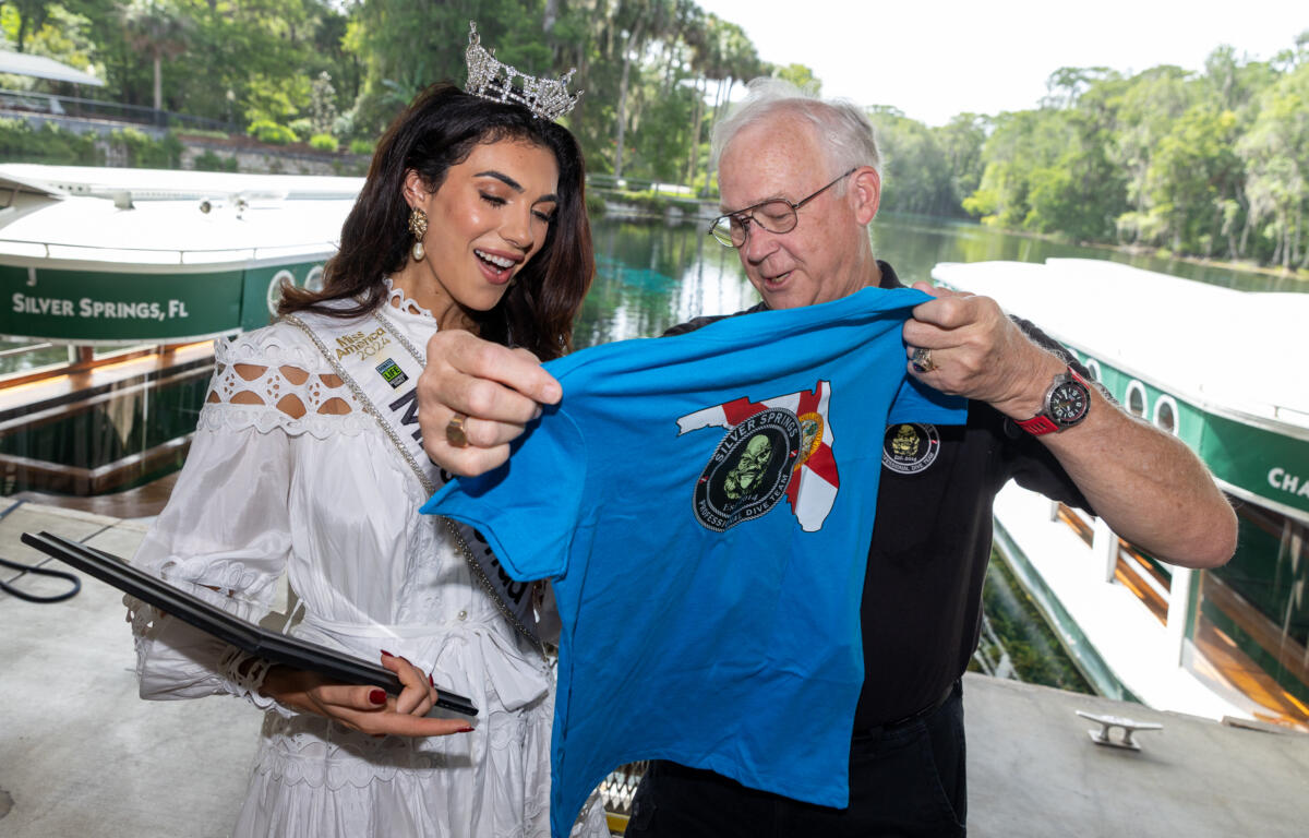 Miss Florida and a man holding up a blue Silver Springs t-shirt near the dock.