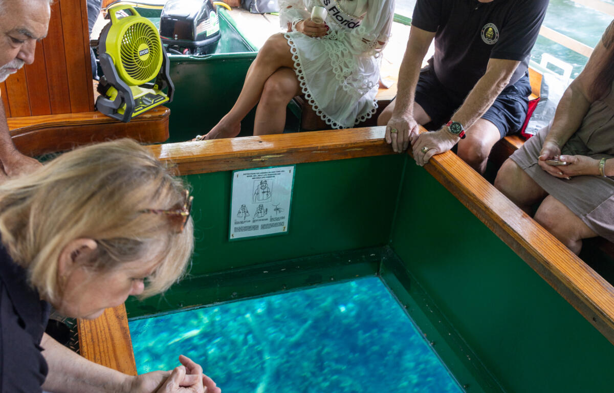 Miss Florida and guests seated around the viewing window of a glass-bottom boat looking into the spring water.