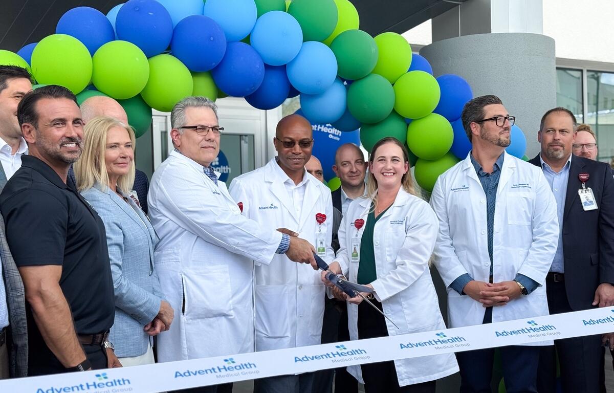 Doctors and staff from AdventHealth Ocala smile as they cut the ribbon in front of a balloon arch at the Medical Office Building grand opening.
