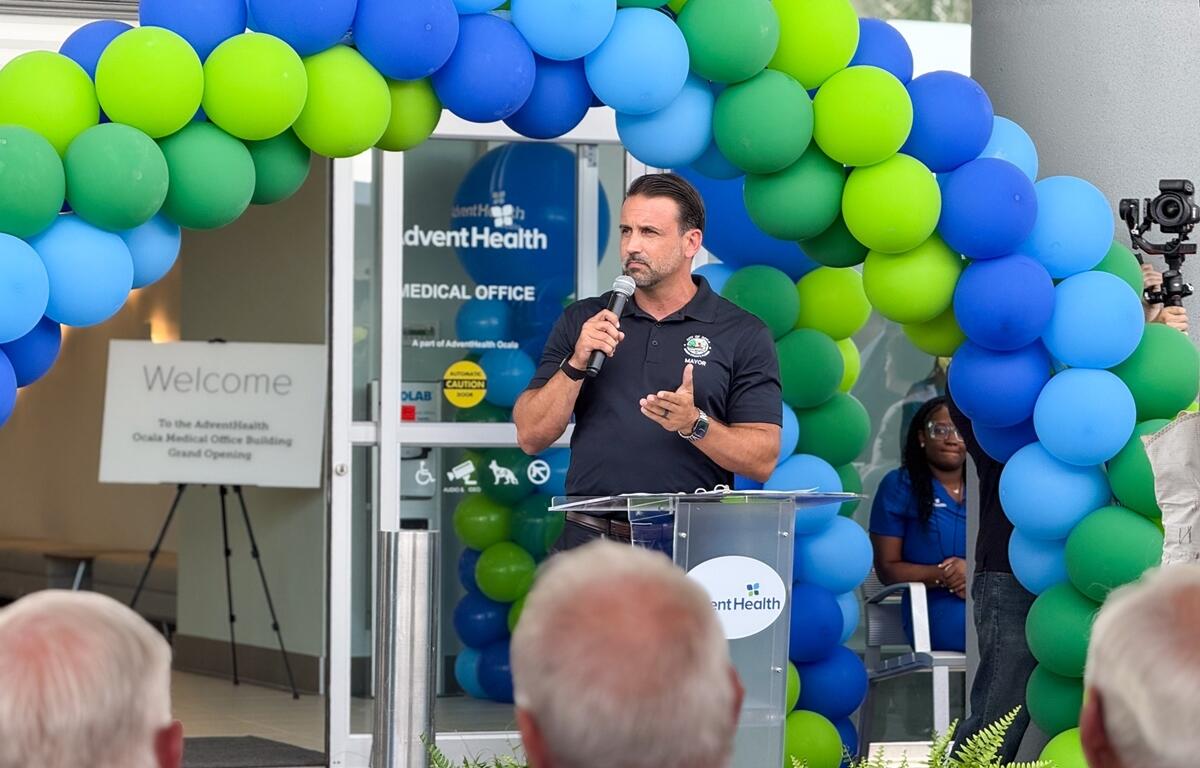 Mayor Ben Marciano speaks at a podium in front of balloon arches during the AdventHealth Ocala Medical Office Building grand opening.