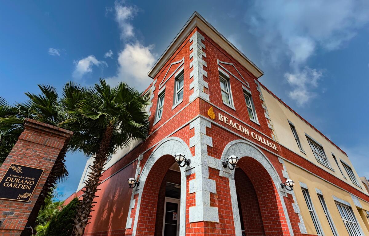 Red brick exterior of Beacon College building in Leesburg, Florida, with arched entryway and palm trees nearby.