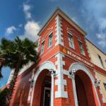 Red brick exterior of Beacon College building in Leesburg, Florida, with arched entryway and palm trees nearby.