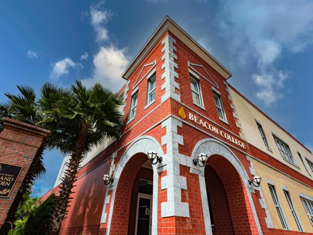 Red brick exterior of Beacon College building in Leesburg, Florida, with arched entryway and palm trees nearby.