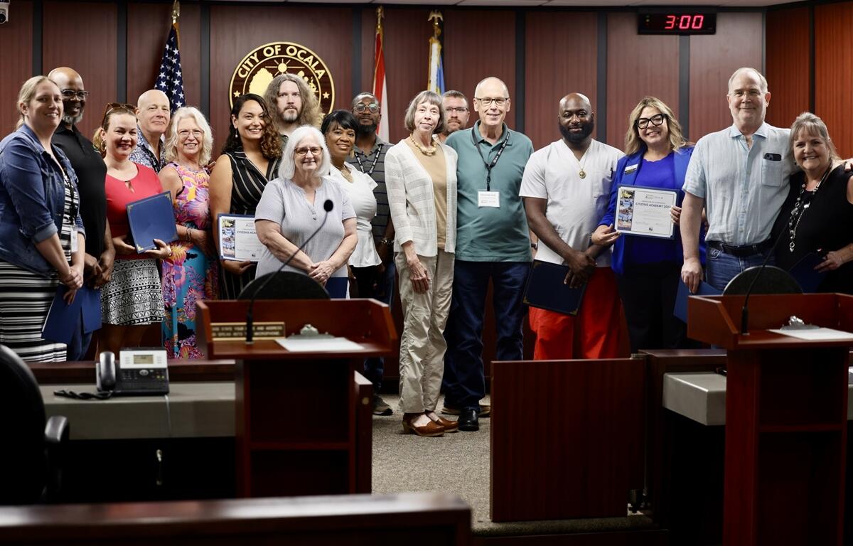 Citizens Academy graduates hold certificates while standing for a group photo in the council chambers.