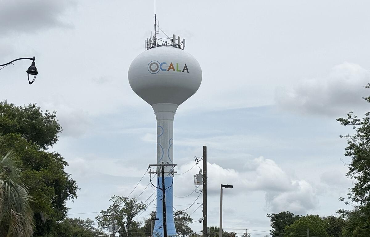 Ocala water tower on a cloudy day, surrounded by trees and utility poles.