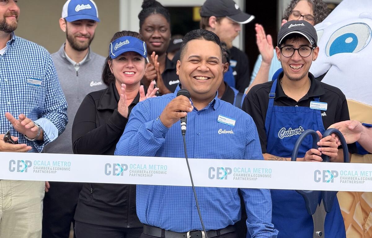 Culver’s employee speaks into a microphone while smiling, surrounded by team members and CEP staff during the ribbon-cutting ceremony at the new Ocala location.