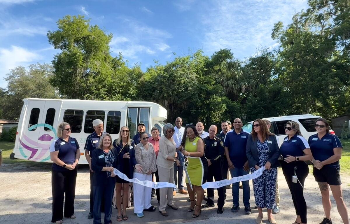 Group of people standing in front of two vehicles during a ribbon cutting event at Estella Byrd Whitman Community Health Center in Ocala.