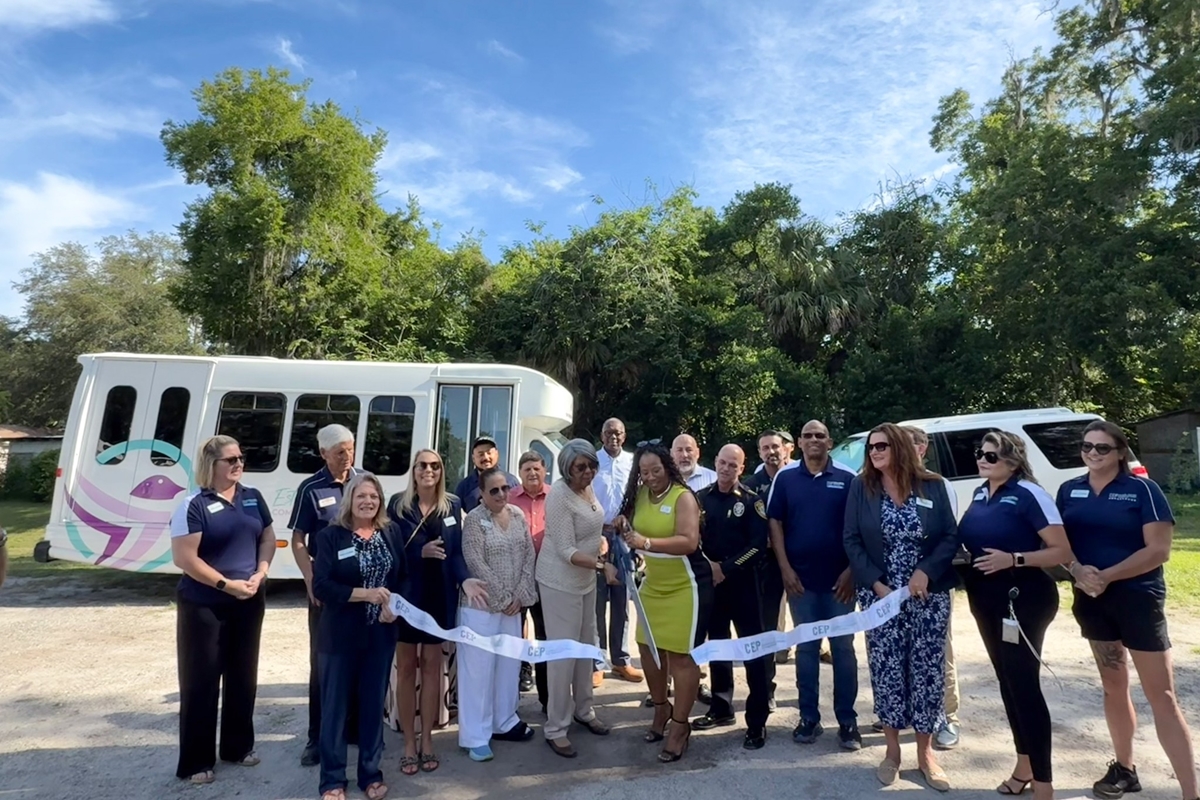 Group of people standing in front of two vehicles during a ribbon cutting event at Estella Byrd Whitman Community Health Center in Ocala.