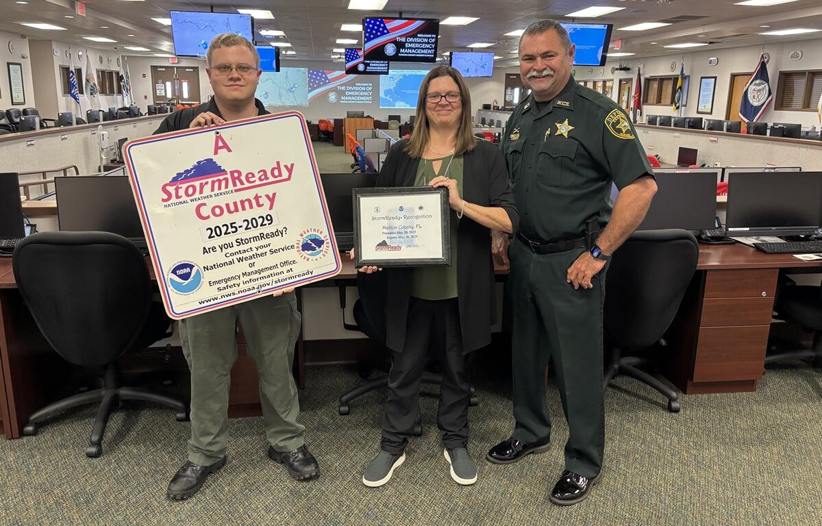 Three Marion County Emergency Management officials hold StormReady certification signage and certificate inside the Emergency Operations Center.