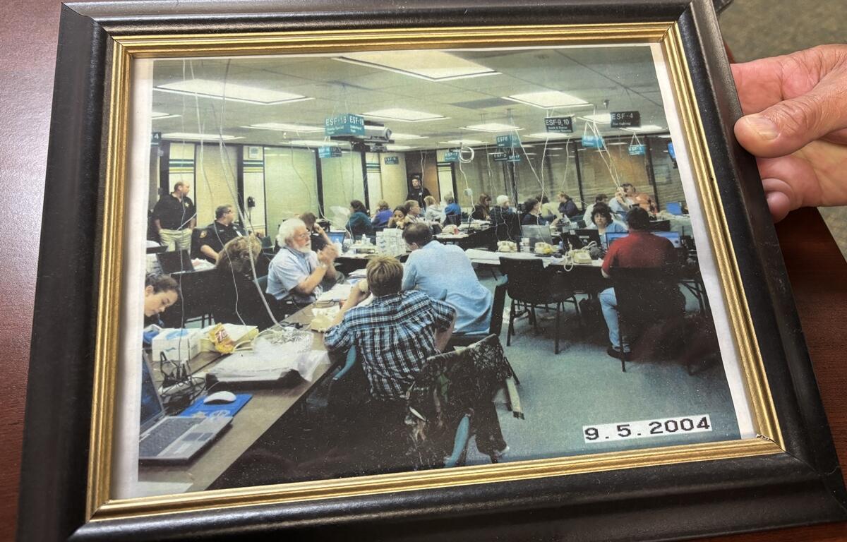 Framed photo of Marion County’s Emergency Operations Center in use during 2004, with people working at tables.