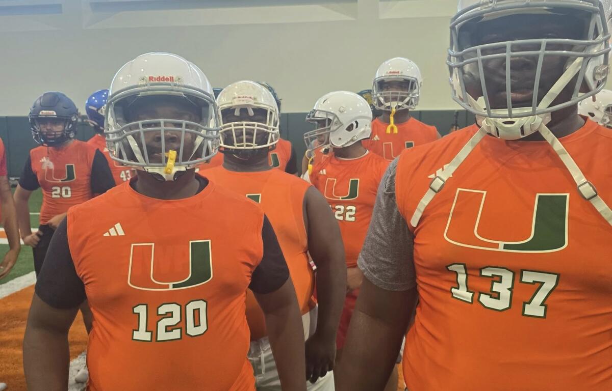 Two young linemen in orange Miami jerseys and helmets stand confidently at the front of a group during a football training session at the Empowered Linemen Academy.