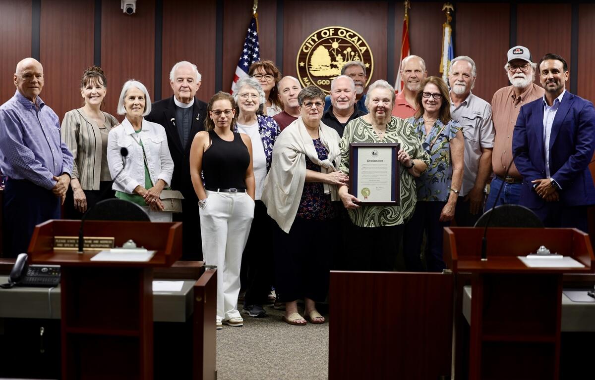 Louine Ek holds a framed proclamation while posing with family members and community supporters.
