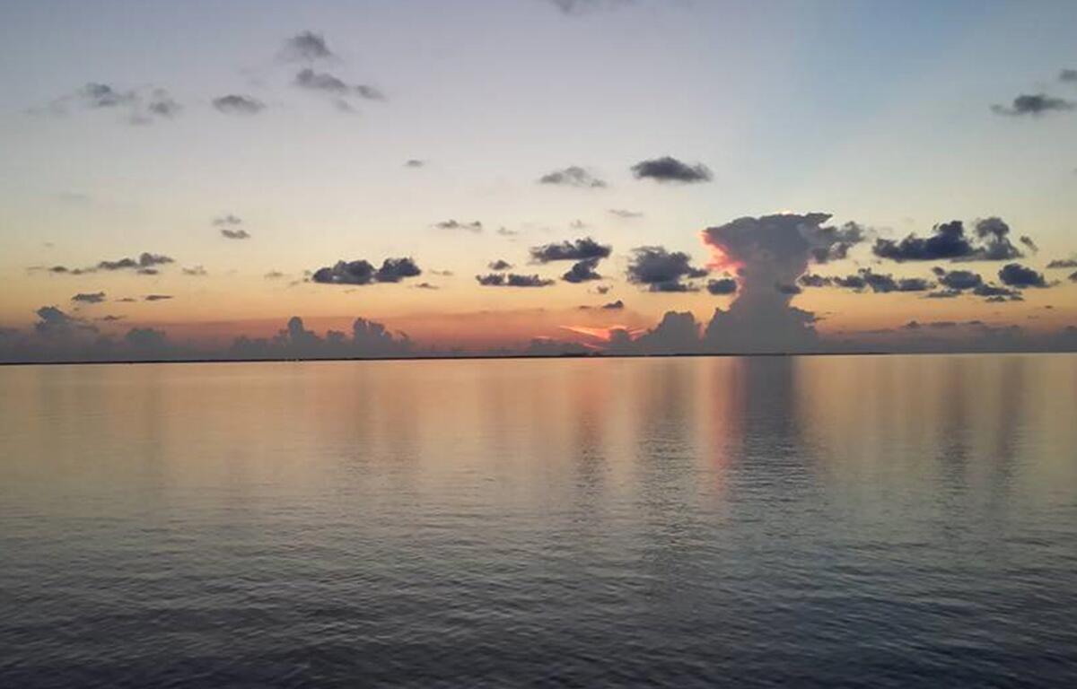 Hazy sunrise over calm Gulf waters with scattered clouds and orange-pink reflections.