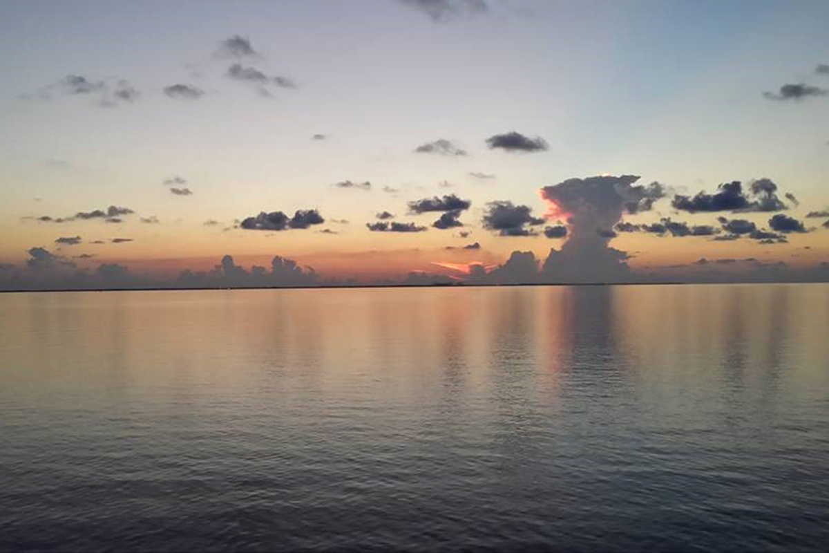 Hazy sunrise over calm Gulf waters with scattered clouds and orange-pink reflections.